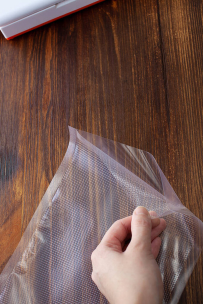 Top view of an empty vacuum bag in a woman's hand on a dark wooden table. Large. Copy space text - Fotó, kép