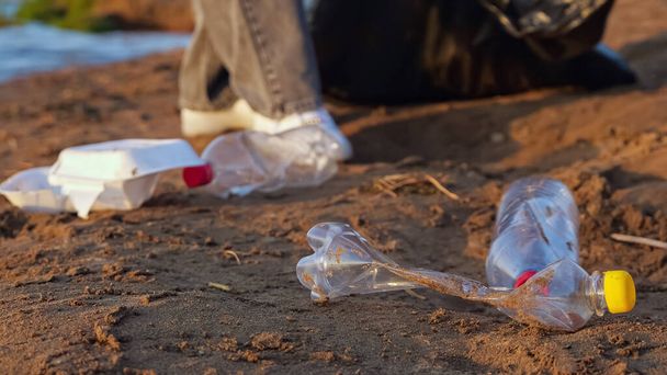 Unrecognizable woman in gloves collects plastic bottles in a black package near the river - Photo, image