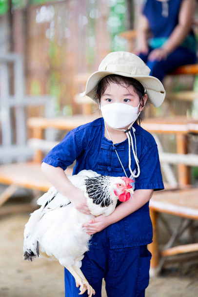 Portrait de petite fille dans un masque 4D blanc tente de tenir un poulet pour la première fois. Les enfants apprennent à cultiver la nature en dehors de la classe. Apprendre des expériences réelles. - Photo, image