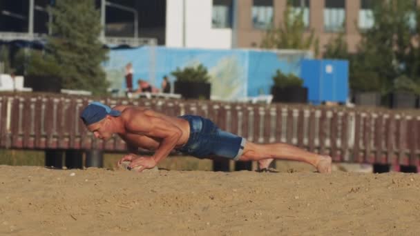 Αθλητικές ασκήσεις σε εξωτερικούς χώρους - νεαρός άνδρας σε φόρμα κάνει push ups από την πέτρα στην παραλία - Πλάνα, βίντεο