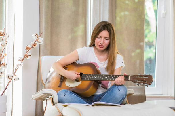 Mladá žena hraje doma na kytaru. Naučit se hrát na hudební nástroj. Záliba ve volném čase. - Fotografie, Obrázek