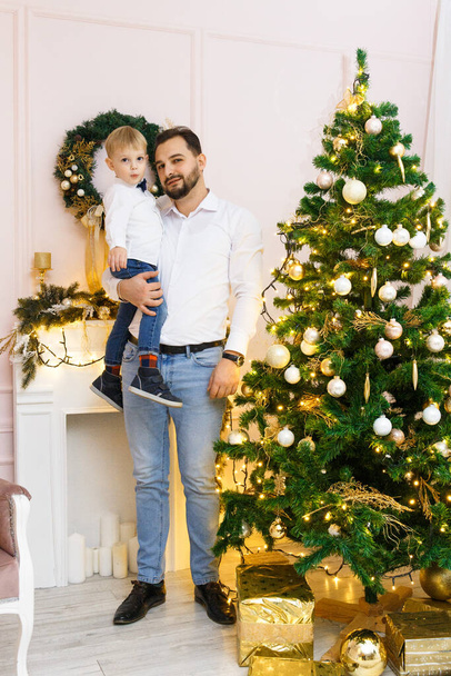 Happy Father and son against Christmas tree with Christmas balls and light garland preparing for celebrating winter holidays: Merry Christmas Eve and Happy New Year 2021. Family concept. - Foto, Imagen