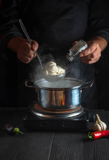 Professionele chef-kok bereidt knoedels in een pan in de keuken van het restaurant. Close-up handen van de kok zout toevoegen - Foto, afbeelding