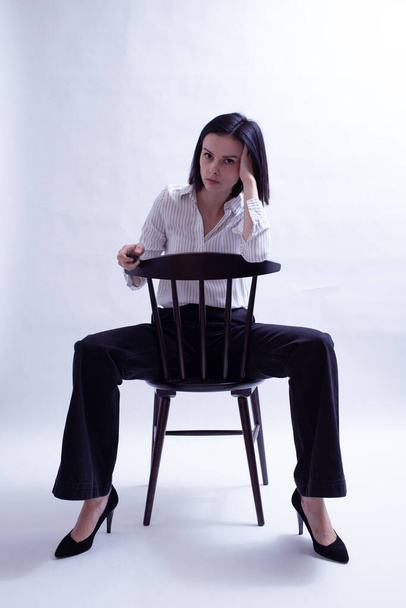 woman in white shirt and black trousers sits on a chair - Zdjęcie, obraz