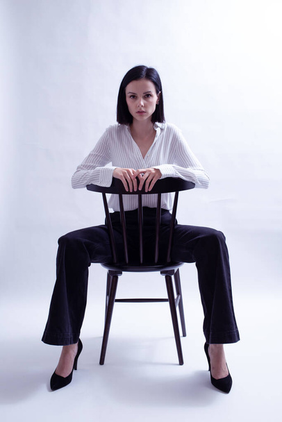 woman in white shirt and black trousers sits on a chair - Foto, Bild