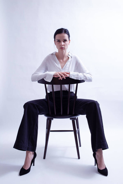 woman in white shirt and black trousers sits on a chair - 写真・画像