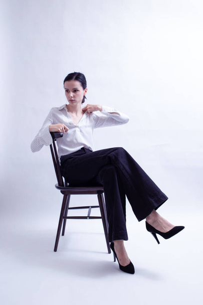 woman in white shirt and black trousers sits on a chair - Valokuva, kuva