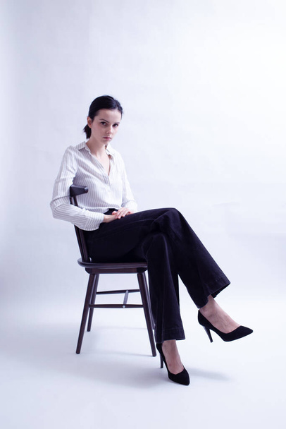 woman in white shirt and black trousers sits on a chair - Photo, image