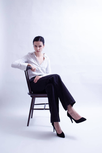 Frau in weißem Hemd und schwarzer Hose sitzt auf einem Stuhl - Foto, Bild
