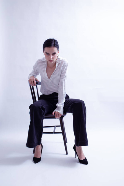 mujer en camisa blanca y pantalones negros se sienta en una silla - Foto, Imagen
