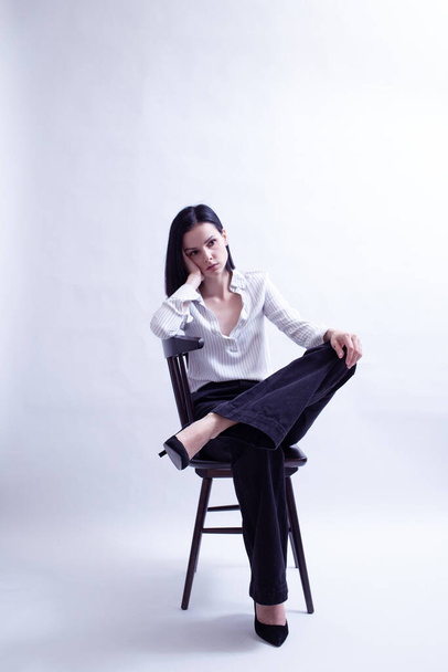 woman in white shirt and black trousers sits on a chair - Foto, imagen