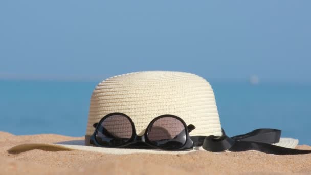 Primo piano di cappello giallo paglierino e occhiali da sole protettivi neri sulla spiaggia sabbiosa al mare tropicale nella calda giornata di sole. Concetto vacanza estiva - Filmati, video