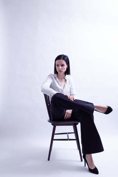 woman in white shirt and black trousers sits on a chair - Foto, immagini