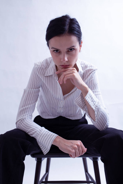 woman in white shirt and black trousers sits on a chair - Foto, afbeelding