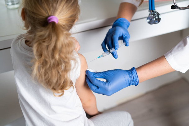 vaccinatie van kinderen, een klein meisje bij een doktersafspraak, een injectie in de arm, de conce. - Foto, afbeelding