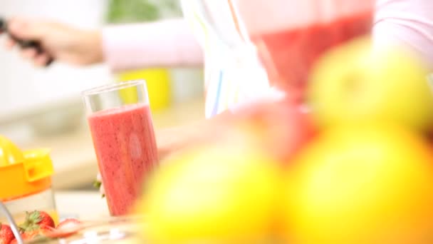 Chica en la cocina añadiendo fresas a la bebida de frutas
 - Metraje, vídeo