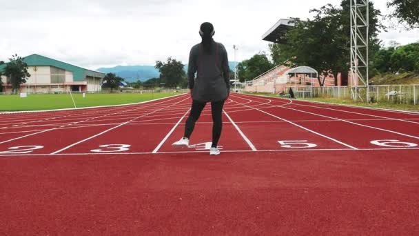 Αθλητική γυναίκα με αθλητικά ρούχα ζεσταίνεται, τεντώνει τους μυς των ποδιών της στην γραμμή εκκίνησης ετοιμάζεται να τρέξει στο τρέξιμο στην αθλητική πίστα. Άσκηση Υγιεινός τρόπος ζωής. - Πλάνα, βίντεο