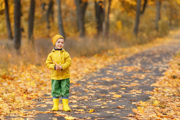 smiling child boy in yellow raincoat and rubber boots in autumn park - Foto, imagen