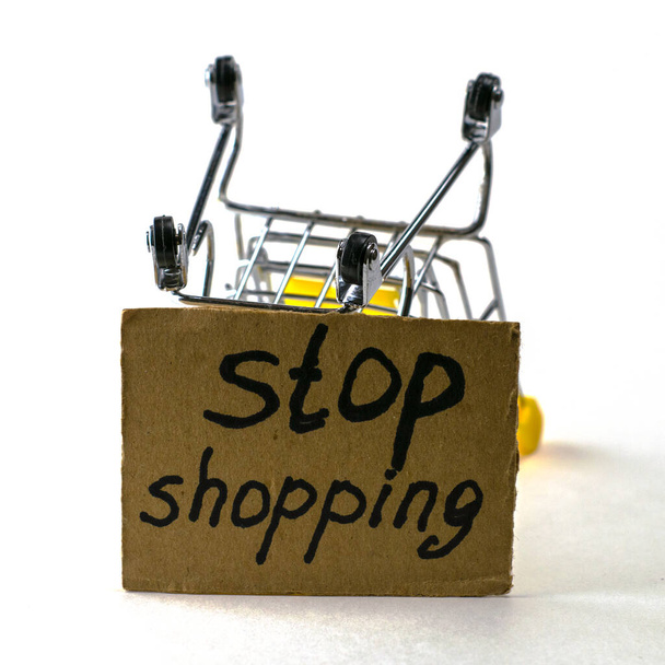 il concetto di rifiuto di acquistare un consumo ragionevole è un carrello della spesa invertito su uno sfondo bianco accanto a un cartello che dice di smettere di fare shopping. Foto di alta qualità - Foto, immagini