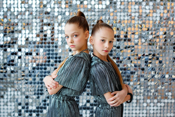 Kaksi teinityttöä seisovat selkä toisilleen hopeisissa futuristisissa haalareissa hopeisen värikkäiden seinien taustalla.. - Valokuva, kuva