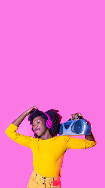 Joven mujer negra bailando escuchando música sosteniendo boombox auriculares inalámbricos sintiéndose libre sonriendo feliz copyspace publicidad aislada - Foto, Imagen