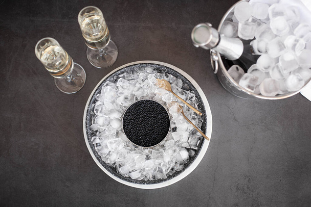 Black caviar in can on ice, champagne in glass and bottle in a bucket - Foto, Imagen