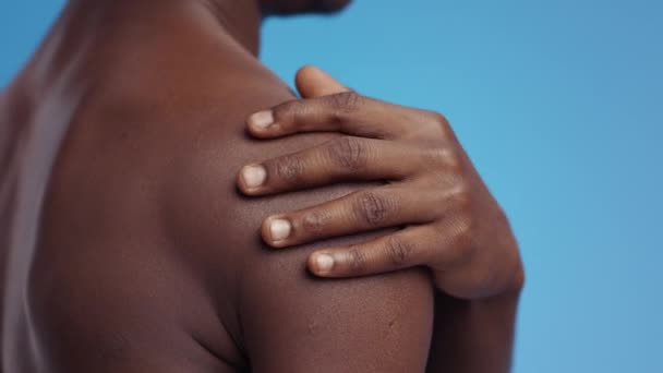 Tunnistamaton afrikkalainen amerikkalainen mies hieromassa tulehtunutta olkapäätään, kärsien lihaskivusta, sinisestä taustasta - Materiaali, video