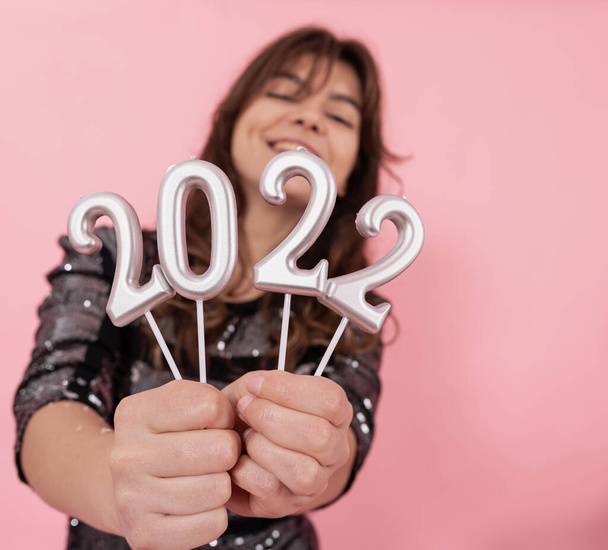 Een vrolijk meisje op een roze achtergrond houdt de nummers 2022 in haar handen. - Foto, afbeelding