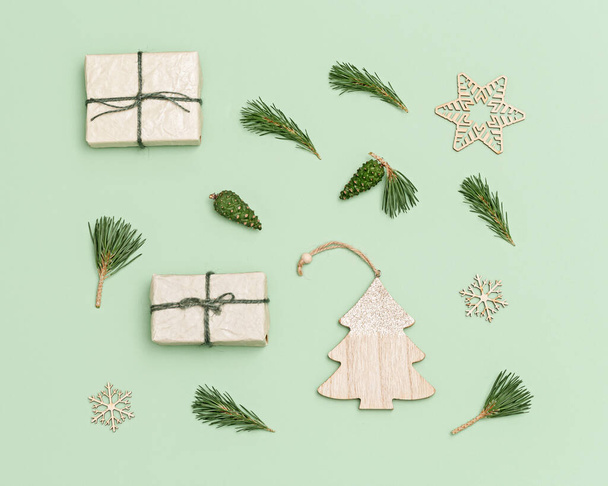 Christmas handmade gifts box or presents decorated with natural fir branches, green pine cones, wooden toys on pastel green background. New Year flat lay with copy space. - Фото, зображення