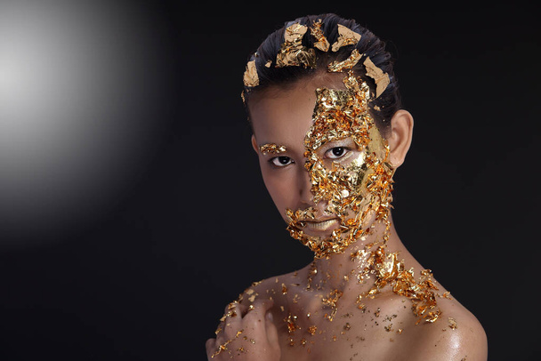 Gold Leaf High fashion style on Asian Woman Face dark mystery look, Golden Mask Facial spa Θεραπεία αντι-γήρανσης νέα διαδικασία, φωτισμός στούντιο μαύρο φόντο καπνού, αντιγραφή χώρου - Φωτογραφία, εικόνα