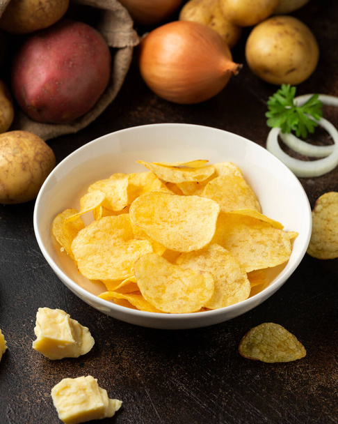 Chipsy ziemniaczane z serem i cebulą w białej misce na rustykalnym tle - Zdjęcie, obraz