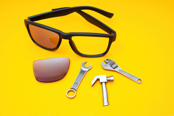 Broken plastic sunglasses with a set of work tools on a yellow background. Repairing accessories at home. - Foto, afbeelding