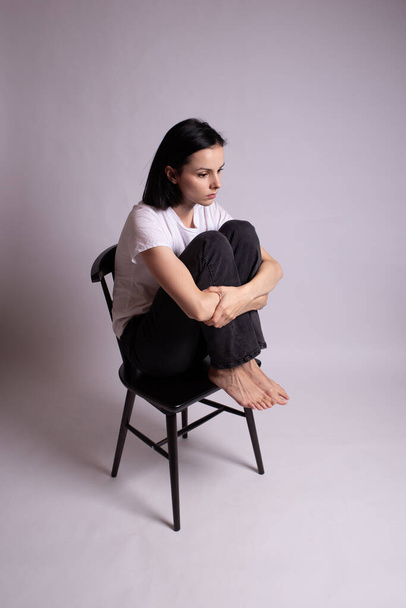 Beyaz tişörtlü kız stüdyoda bir sandalyede oturuyor. - Fotoğraf, Görsel