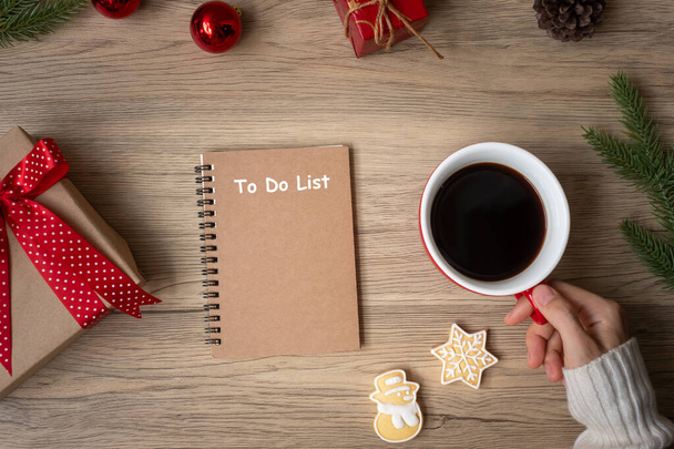 Woman hand holding black coffee cup with blank notebook and Christmas cookies on table. Xmas, Happy New Year, Goals, Resolution, To do list, Strategy and Plan concept - Photo, Image