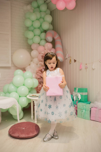 мила маленька дівчинка в пухнастій сукні стоїть з подарунком в новорічних прикрасах
 - Фото, зображення