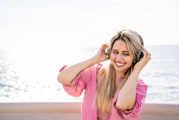 Békés nő zenét hallgat fülhallgatóban a tengerparton. - Fotó, kép