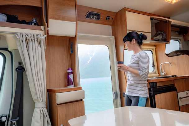 Woman in the interior of a camper RV motorhome with a cup of coffee looking at nature. Family vacation travel RV, holiday trip in motorhome, Caravan car Vacation. - Foto, immagini