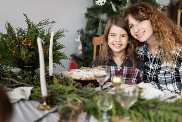 Család karácsonykor az ünnepi asztalnál. Egy boldog anya és lánya portréja egy díszített asztalnál a nappaliban. Gyertyák, ágak - Fotó, kép