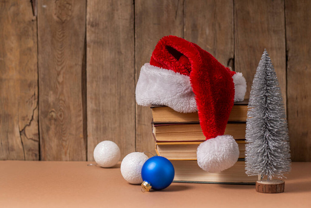 木の背景に本、クリスマスの装飾やサンタクロースの帽子のスタック. - 写真・画像