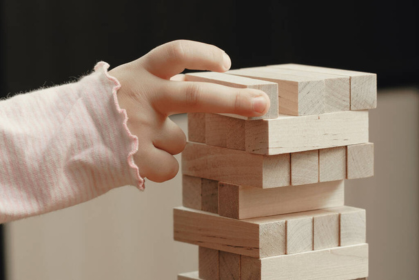 The hands of a child playing a board game, builds a tower from wooden blocks. - 写真・画像
