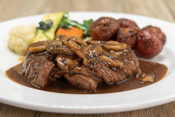 Steak de filet mignon trempé recouvert de champignons dans une assiette et servi avec pommes de terre et légumes rôtis pour un dîner gastronomique. - Photo, image