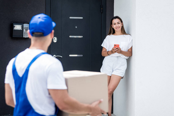 Young courier delivering goods to a young woman at home - Foto, immagini