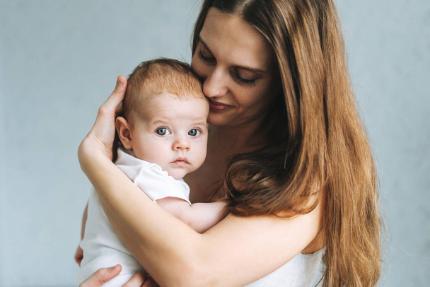 Retrato de jovem mãe com cabelos longos segurando bebê menina em mãos em casa - Foto, Imagem