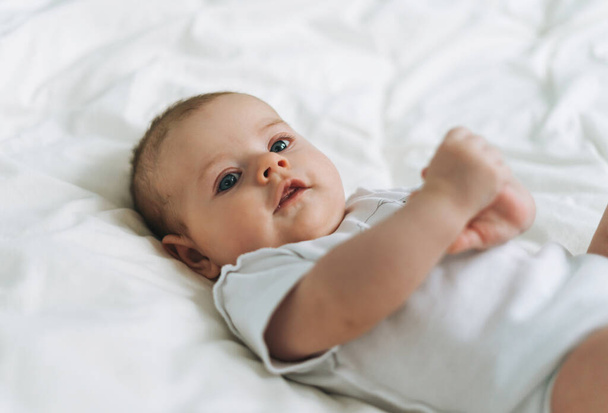 Симпатичная девочка 2-4 месяца на кровати с белым бельем, натуральными тонами, выборочным фокусом - Фото, изображение