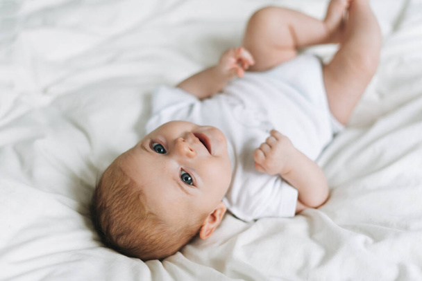 Cute baby girl 2-4 month on the bed with white linen, natural tones, selective focus - Foto, imagen