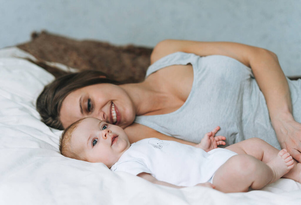 Fiatal anya szórakozás aranyos kislány az ágyon, természetes tónusok, szerelem érzelem - Fotó, kép