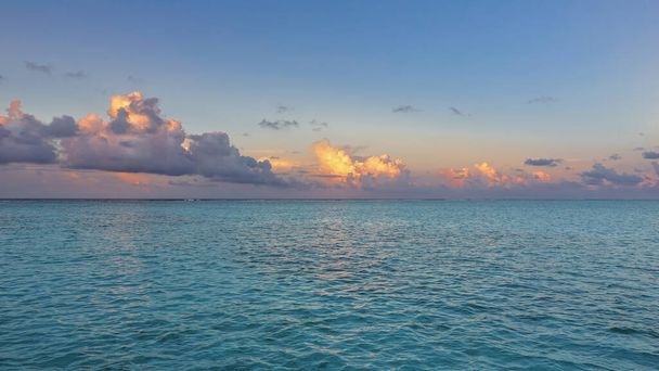 アクアマリン海の表面には波紋があります。青空には青、金、ピンクの雲があります。モルディブの静かな夜. - 写真・画像