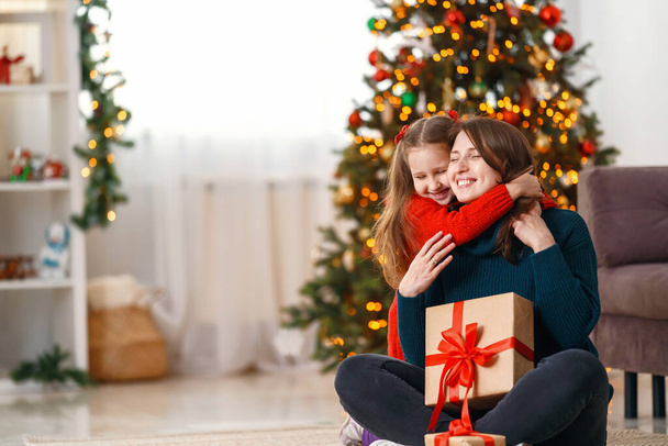 Merry Christmas and Happy Holidays Happy mom and daughter hugging, and hold with christmas gift box on background Christmas tree decorated with a garland. Copy space - Фото, зображення