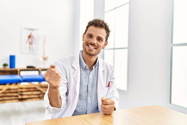 Fizyoterapist üniforması giyen genç İspanyol adam klinikte stres önleyici topa basıyor. - Fotoğraf, Görsel