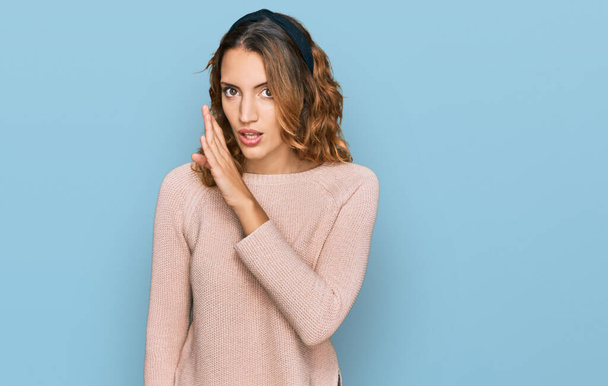 Beautiful young caucasian woman wearing casual sweater hand on mouth telling secret rumor, whispering malicious talk conversation  - Photo, Image